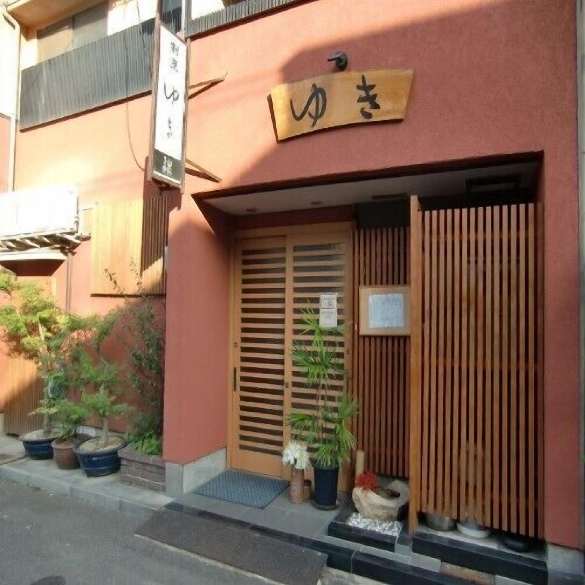 A building with a wooden door and a sign above it. There are potted plants outside.