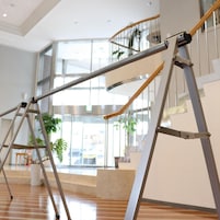 Un interior moderno con piso de madera, una escalera con barandilla de vidrio y vistas al exterior a través de amplios ventanales.