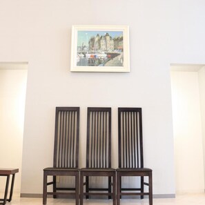 A framed cityscape painting above three dark wooden chairs against a plain wall. - Imabari Urban Hotel (Imabari)