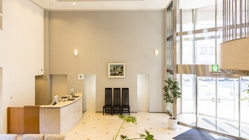 Zona de recepción con mostrador, asientos, un cuadro en la pared y una planta en maceta.