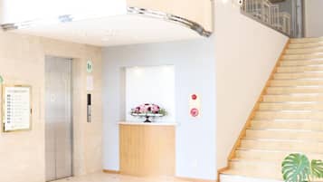 A hotel lobby with a reception desk, a staircase, and an elevator.