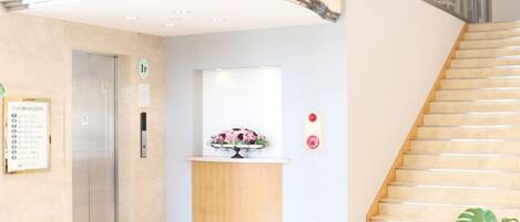 A hotel lobby with a reception desk, a staircase, and an elevator.