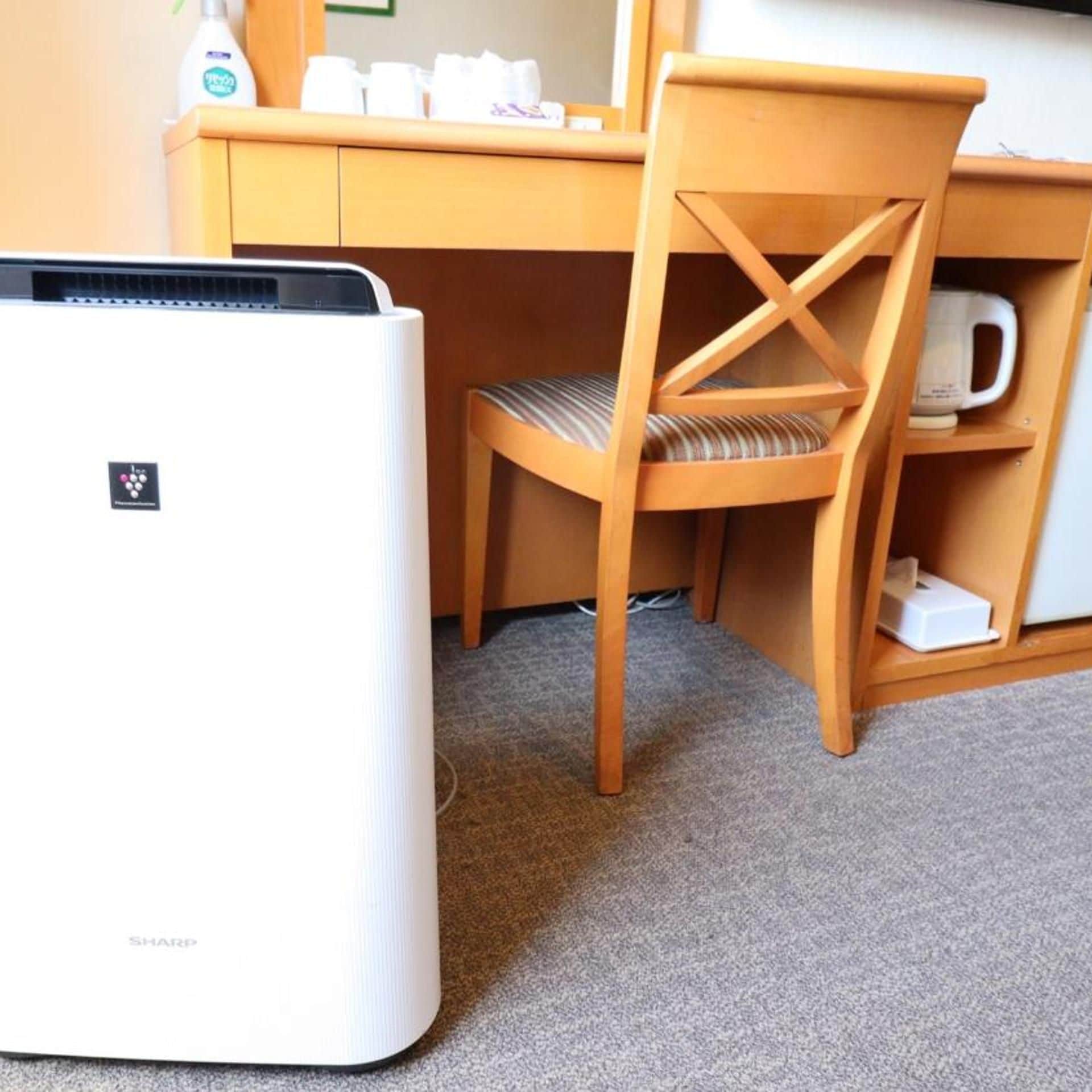 A room with a white Sharp refrigerator, a wooden desk with a chair, and a coffee maker on the shelf.