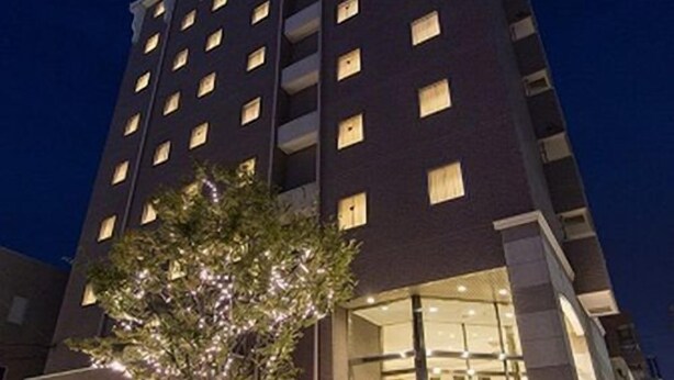 Et flere etagers hotel med oplyste vinduer og et træ med lys foran.
