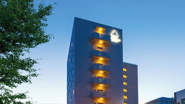 Een hoog gebouw met verlichte ramen en een driehoekig waarschuwingsbord aan de bovenkant.
