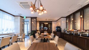 Een ruime eetruimte met een lange houten tafel en verschillende stoelen, een keuken met een buffet, en een groot raam met gordijnen.