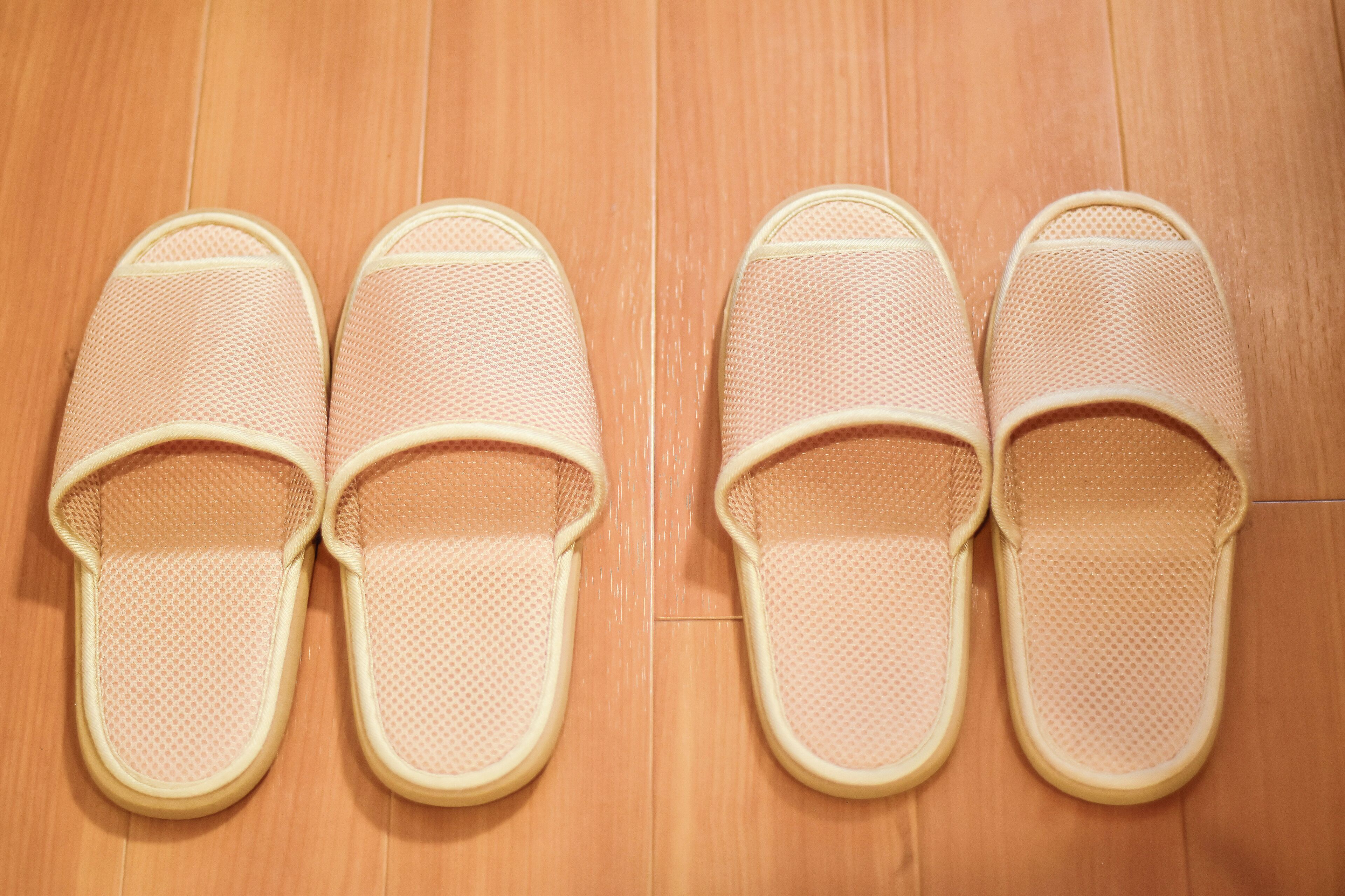 A pair of pink slippers with a textured surface, placed on a wooden floor.