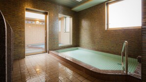 Een badkamer met een hottub in een glazen omhulsel, betegelde wanden en een raam.