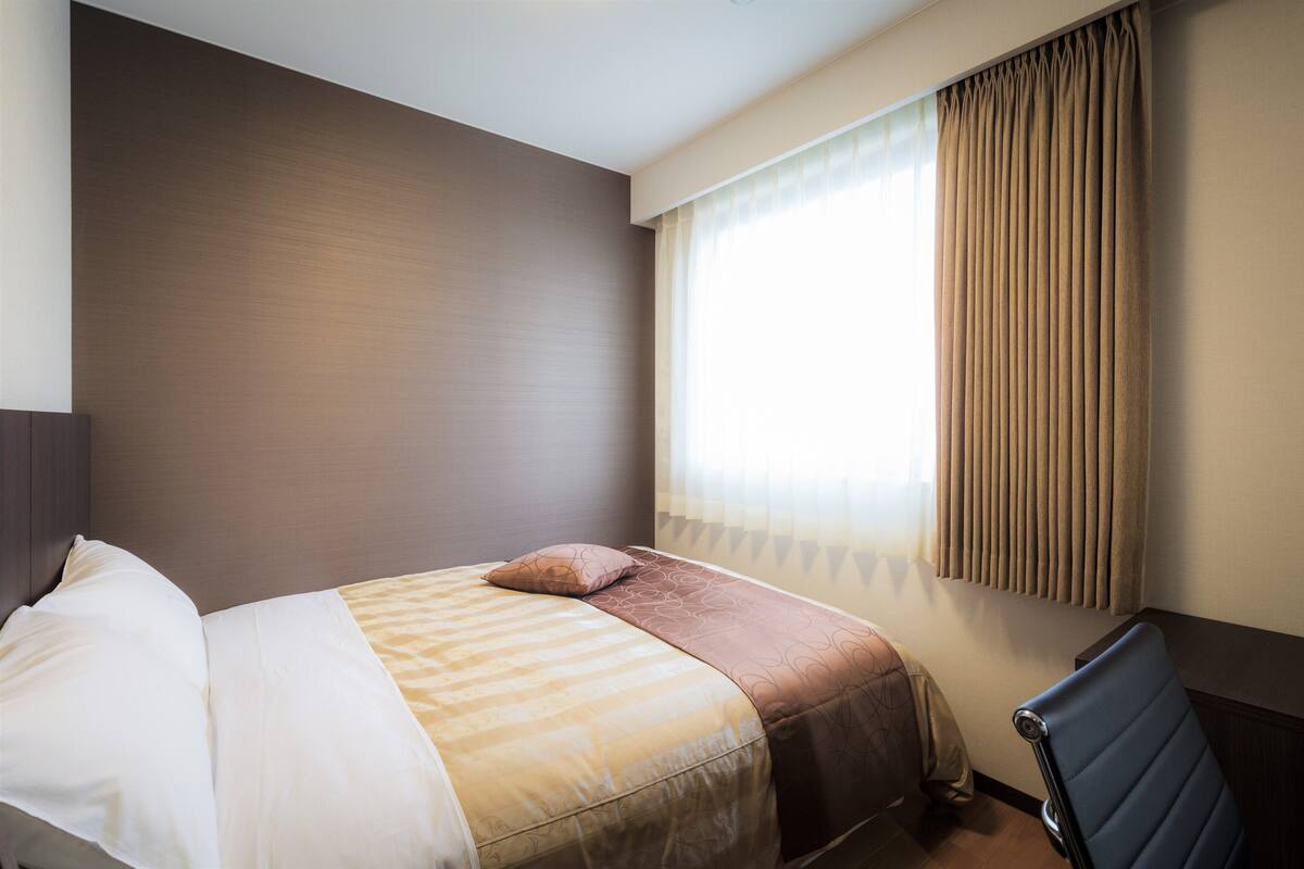 Een hotelkamer met een bed, een stoel en een raam met gordijnen.