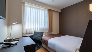 Hotelkamer met een bed, bureau, stoel, raam met gordijnen en een wandlamp.