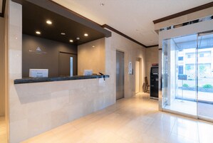 Zona de recepción de hotel con mostrador, pantalla digital y puerta de cristal.