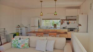 A compact kitchen with white cabinets, a dining area with a wooden table, and a sofa with patterned cushions. - Terrace House Yamabare (Ishigaki)