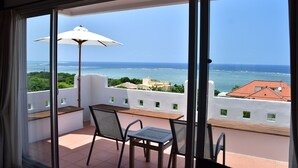 A balcony with a table and chairs, overlooking a coastal view with buildings and greenery. - Terrace House Yamabare (Ishigaki)