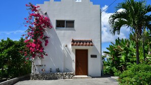 A white building with a wooden door, a small window, and a tiled roof. - Terrace House Yamabare (Ishigaki)