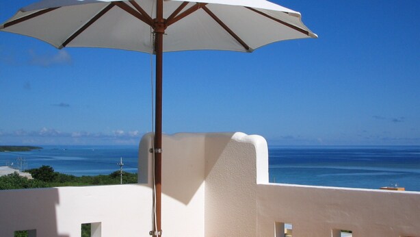 A white umbrella on a wooden deck with a view of the ocean. - Terrace House Yamabare (Ishigaki)