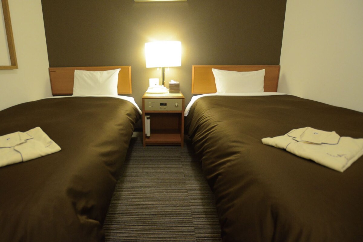 A hotel room with two beds, a nightstand, a lamp, and a mirror.