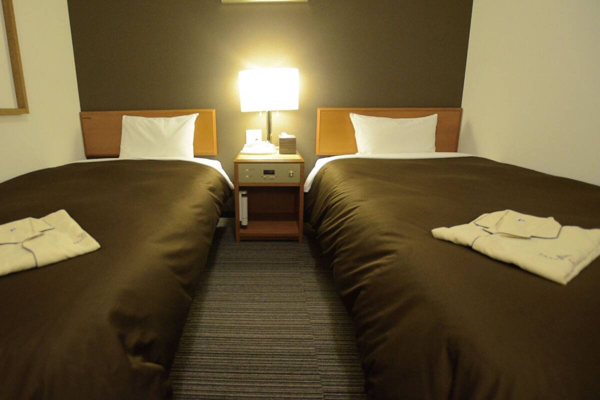 Habitación de hotel con dos camas, una mesita de noche, una lámpara y un espejo.