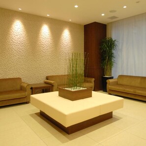 Eine moderne Lobby mit einer Rezeption, zwei Sofas, einem Couchtisch mit Pflanze und einer strukturierten Wand.