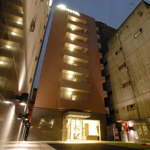 Un hotel con fachada moderna, varios balcones y una entrada bien iluminada.