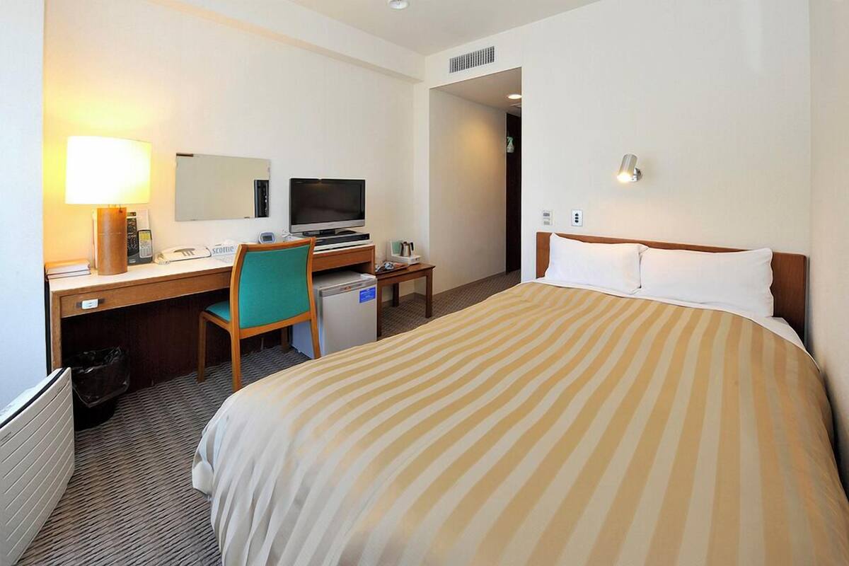 Ein Hotelzimmer mit Bett, Schreibtisch, Stuhl, Fernseher und einer kleinen Küchenzeile.