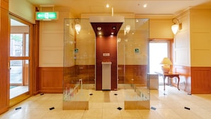 A reception area with a glass elevator, a reception desk, and a door leading outside. - Hotel Gimmond Kyoto (Kyoto)