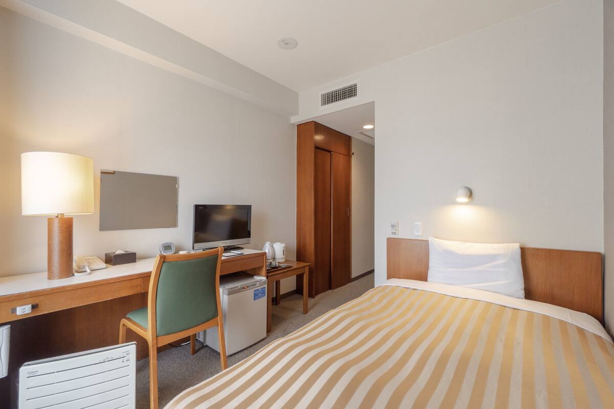 Ein Hotelzimmer mit Bett, Schreibtisch, Stuhl, Fernseher und kleinem Kühlschrank.