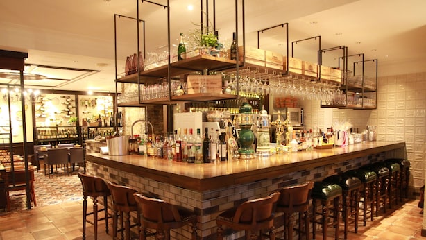 A bar area with a long counter, multiple stools, and shelves stocked with bottles and glasses. - Hotel Gimmond Kyoto (Kyoto)
