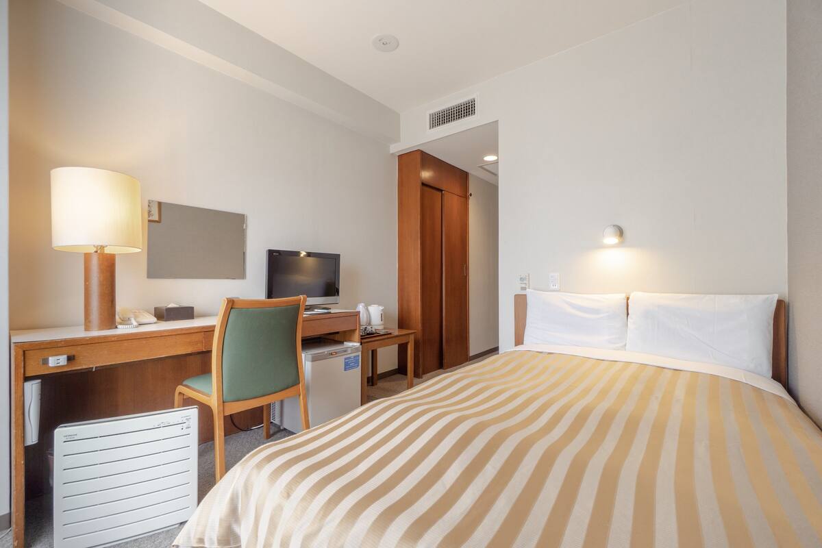 Ein Hotelzimmer mit Bett, Schreibtisch, Stuhl, Fernseher und einer kleinen Küchenzeile.