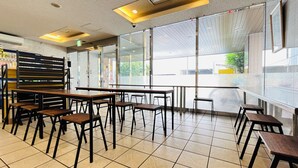 A modern restaurant interior with high ceilings, large windows, and a mix of wooden and metal furniture. - R-bend Hotel ATSUGI (Atsugi)