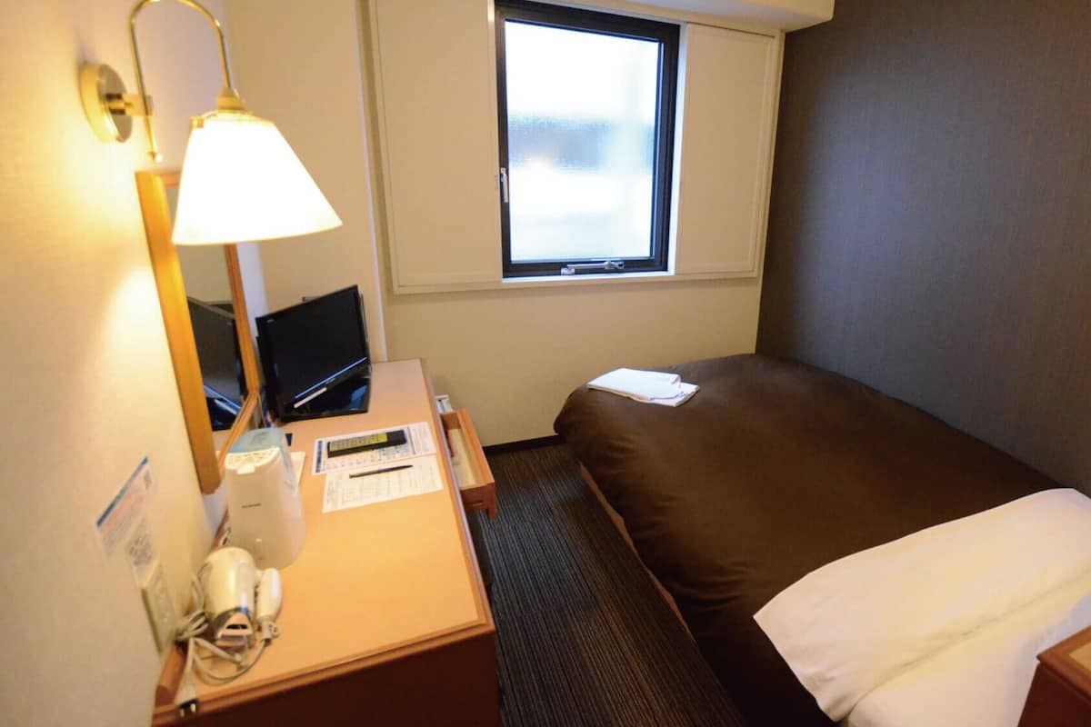 Une chambre d’hôtel avec un lit, un bureau équipé d’un ordinateur, un téléphone et une fenêtre.