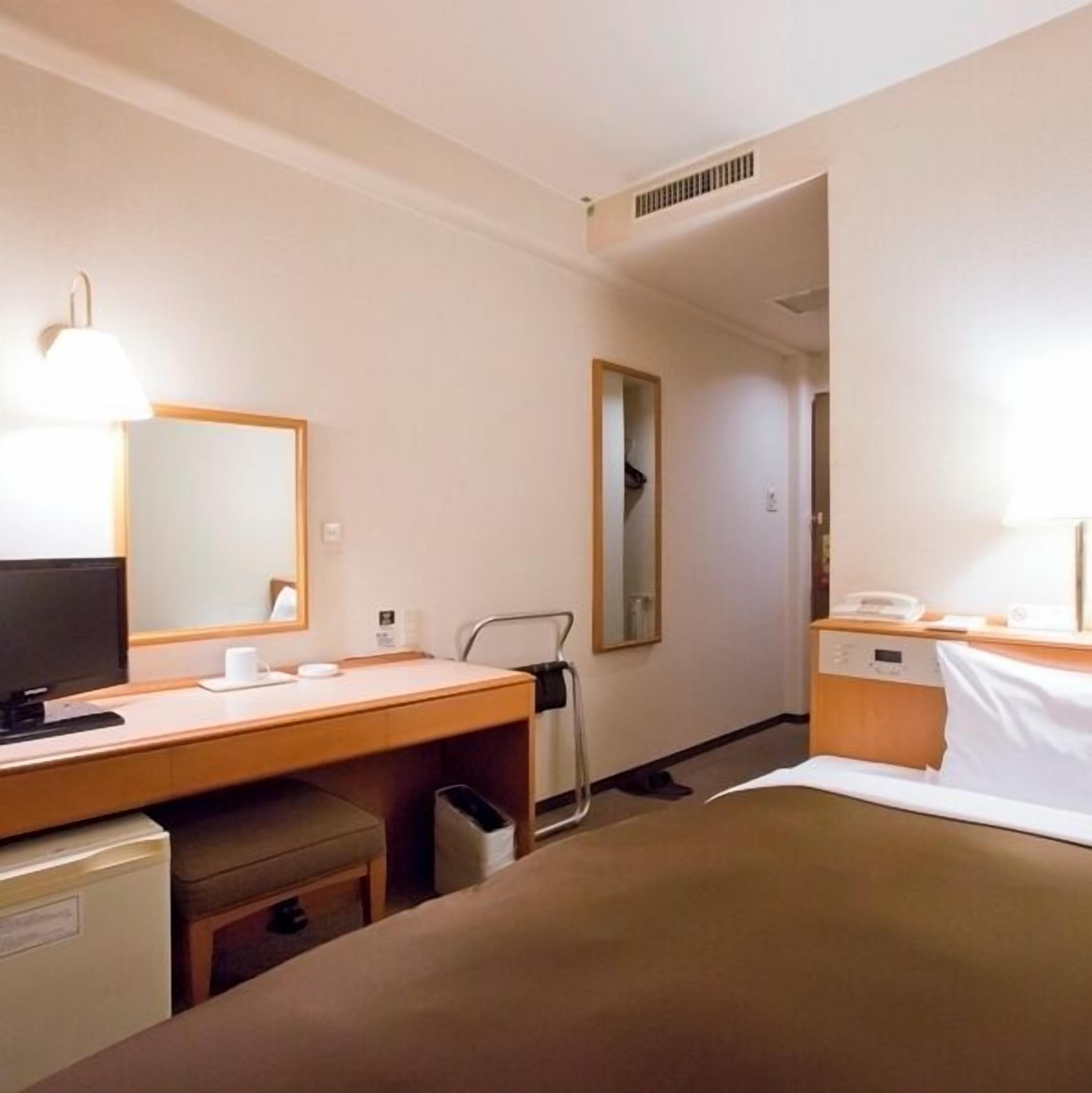 Hotellihuone, jossa on sänky, työpöytä tietokoneella, televisio, peili ja yöpöytä lampulla.