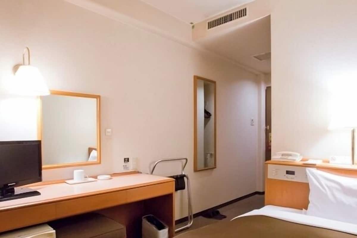 Une chambre d’hôtel comprenant un lit, un bureau avec un ordinateur, une télévision, un miroir et une table de chevet avec une lampe.
