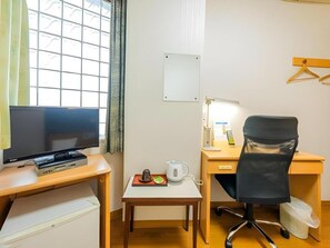 A compact hotel room with a television, a desk with a chair, a small table with a kettle, and a window with blinds. - Mimatsu Hotel (Mito)