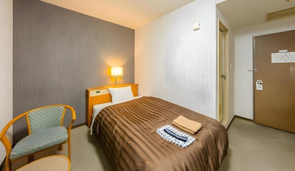 A hotel room with a bed, a chair, a bedside table, and a door. - Mimatsu Hotel (Mito)