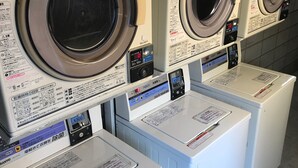 A row of front-loading washing machines with control panels and instruction labels. - Mimatsu Hotel (Mito)