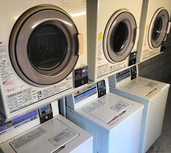 A row of front-loading washing machines with control panels and instruction labels. - Mimatsu Hotel (Mito)