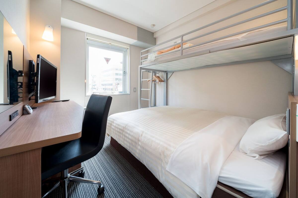 Une chambre d’hôtel de taille réduite, équipée d’un lit superposé, d’un bureau avec un ordinateur et d’une chaise.