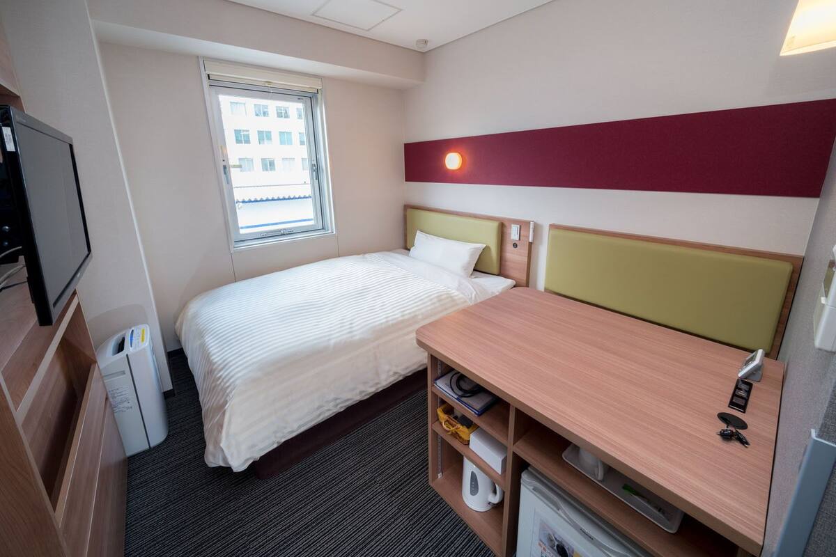 Une chambre d’hôtel équipée d’un lit, d’un bureau, d’une télévision, d’une fenêtre et offrant une vue sur l’extérieur.