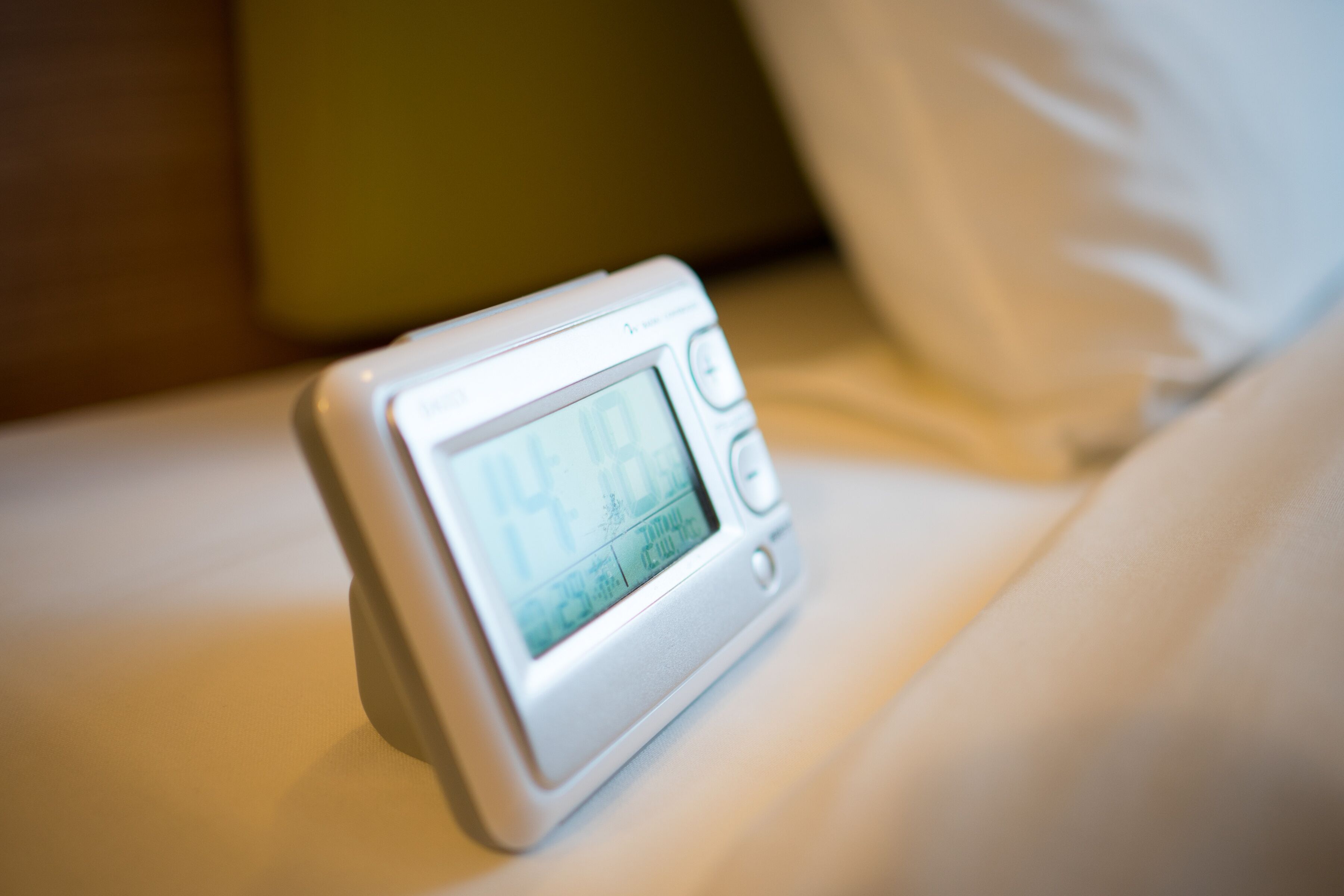 A digital clock on a bedside table in a hotel room.