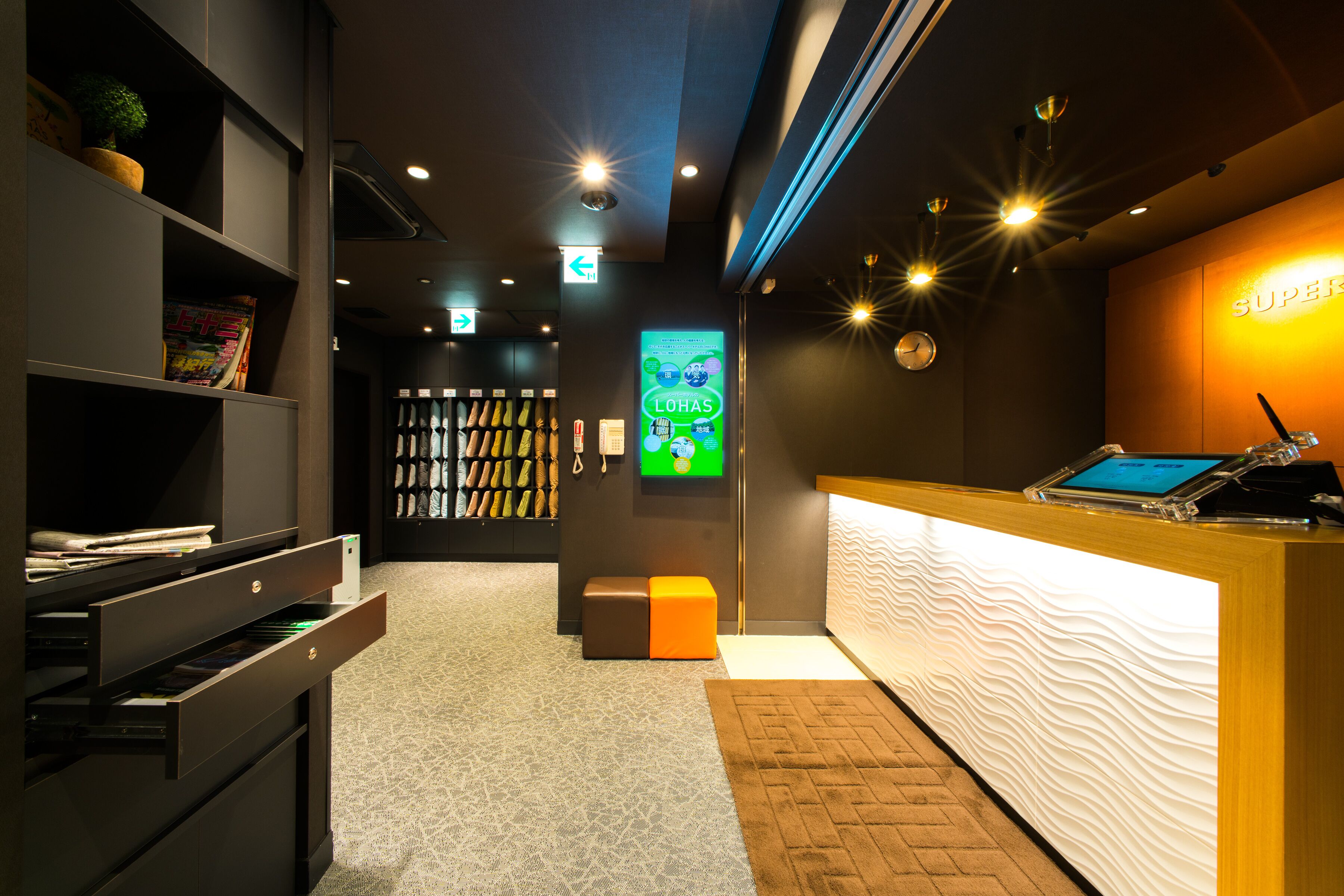 A reception area with a wooden desk, a digital screen, and a wall-mounted clock.