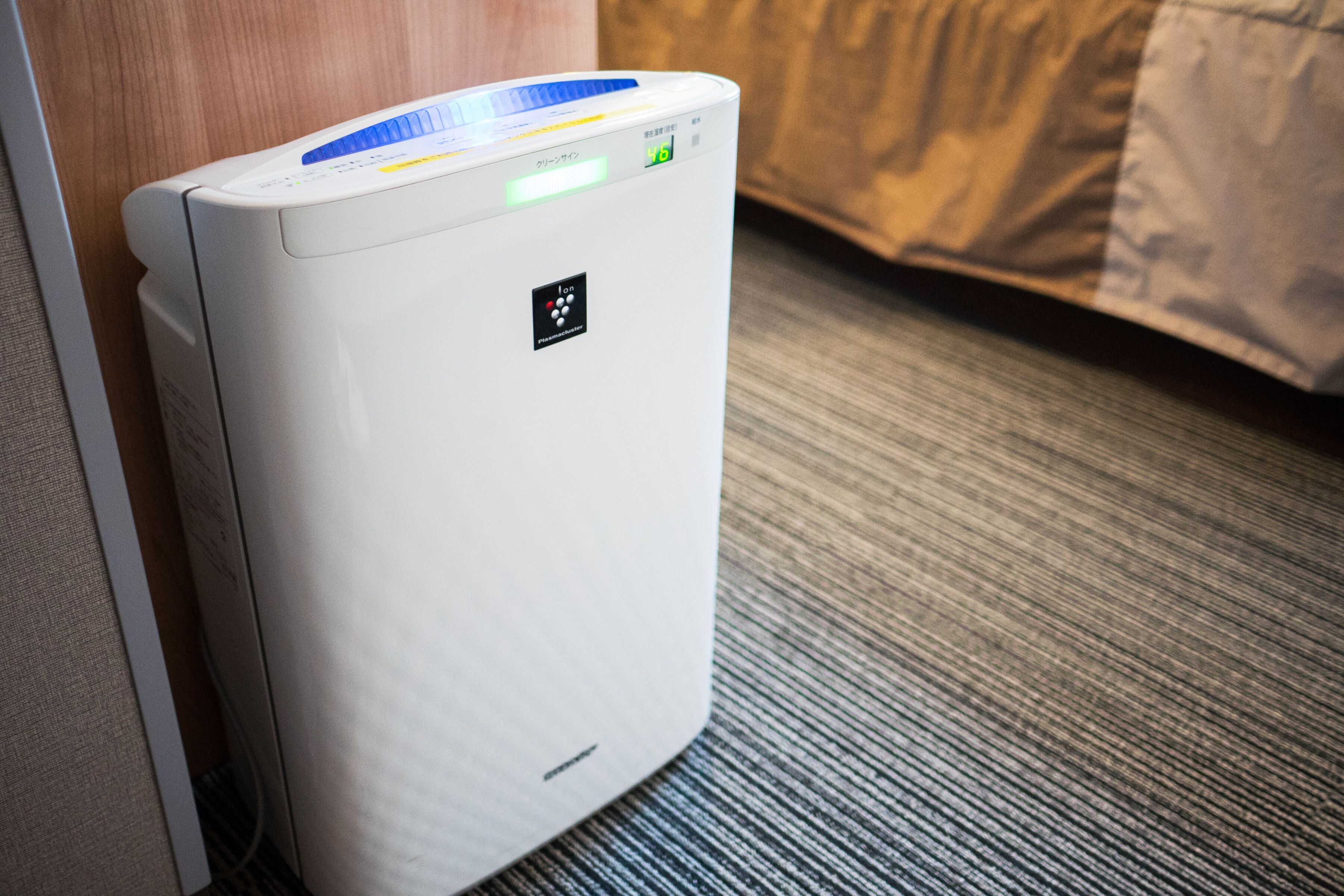 A white portable heater with a digital display and buttons on top, placed on a textured carpet near a wooden door.