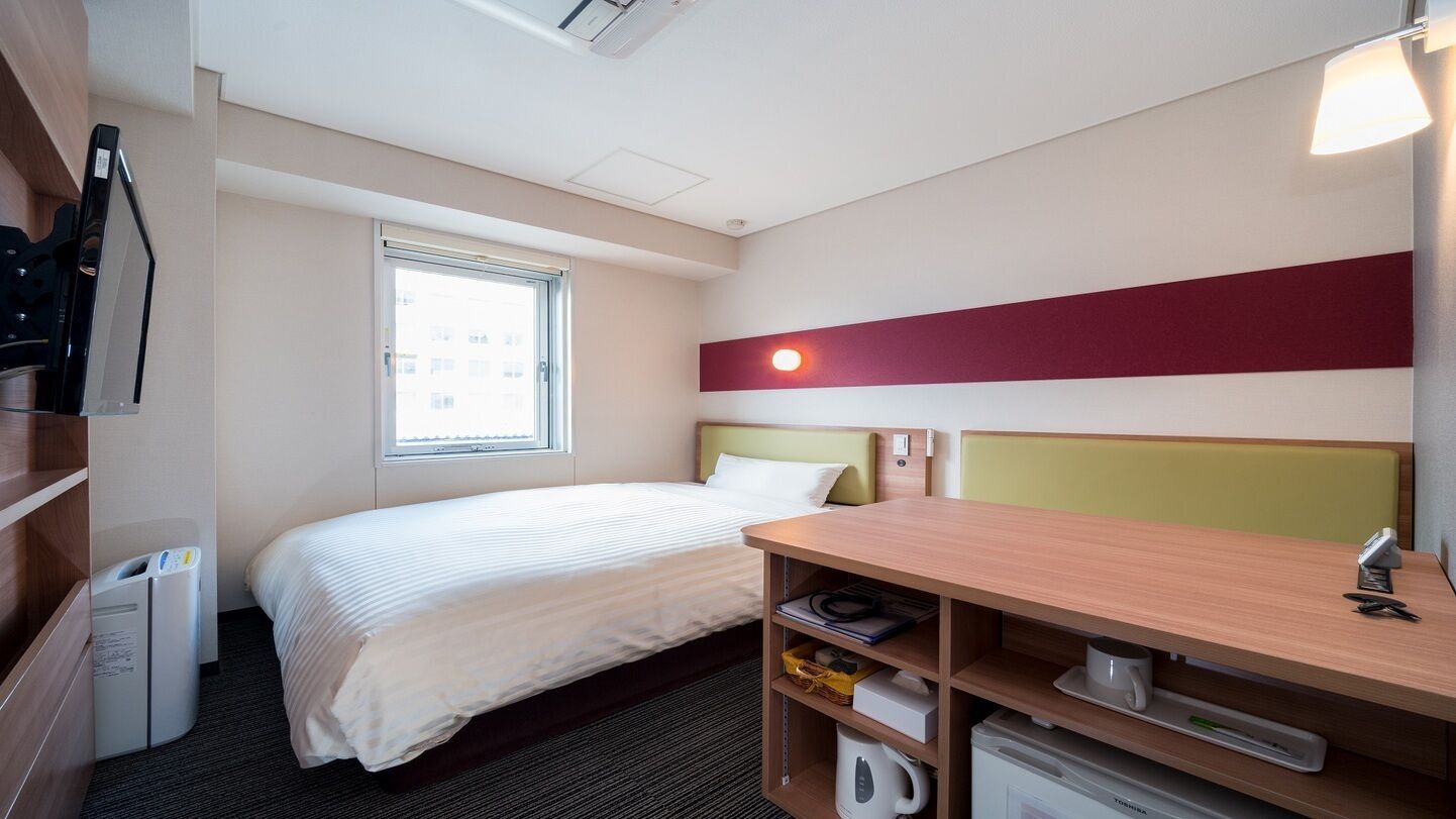 Une chambre d’hôtel avec un lit, un bureau, une fenêtre et un mini-bar.