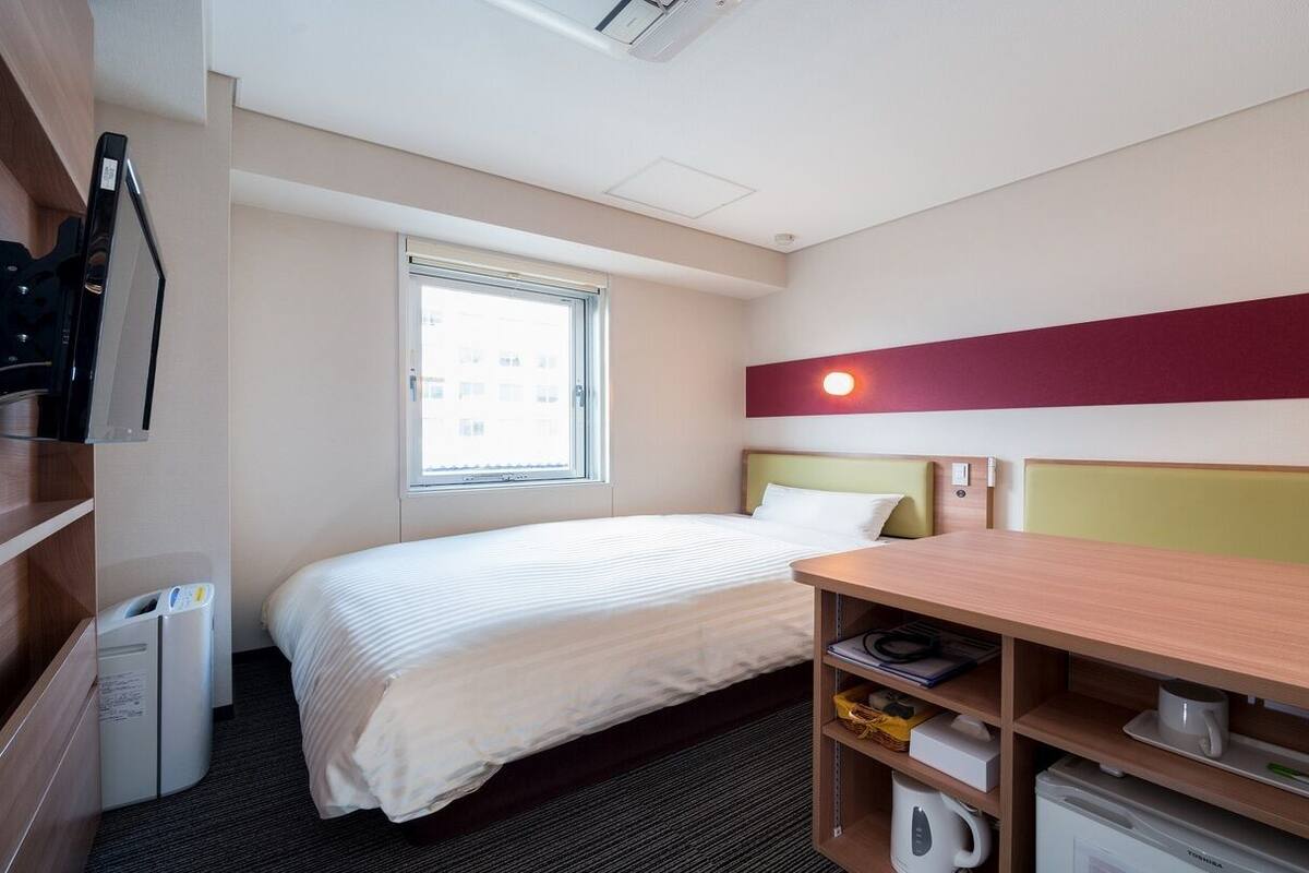 Une chambre d’hôtel avec un lit, un bureau, une fenêtre et un mini-bar.