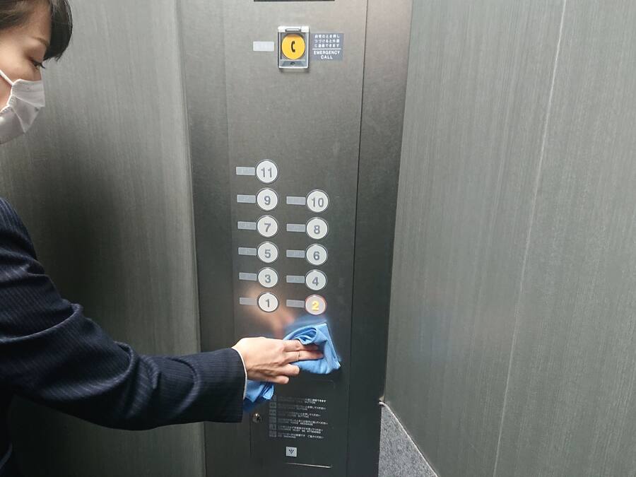 Eine Person reinigt ein Bedienelement einer Aufzugskabine mit einem blauen Tuch.