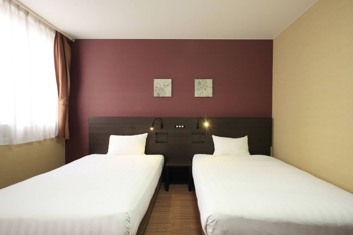 A hotel room with two single beds, a wooden headboard, a nightstand, and two wall-mounted lamps.