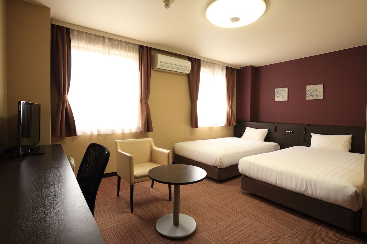 A hotel room with two beds, a desk, a chair, and a small table.