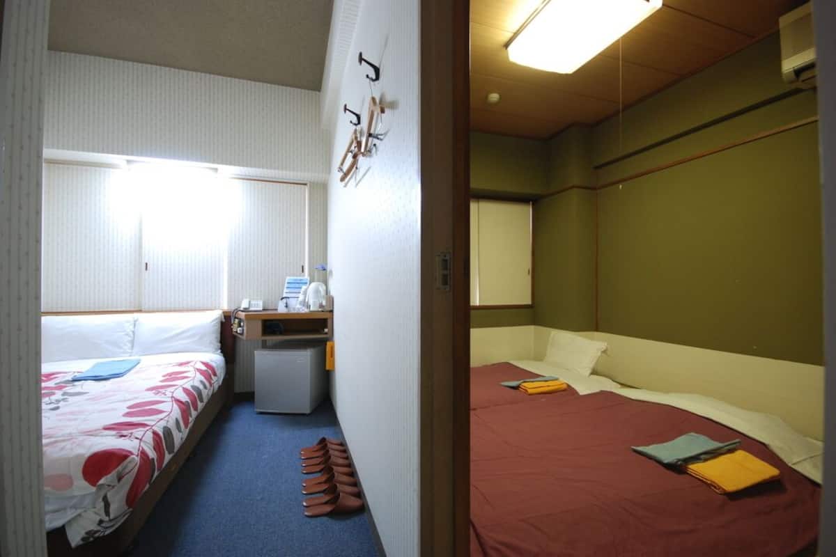 A room with two beds, a desk, a chair, and a small refrigerator.