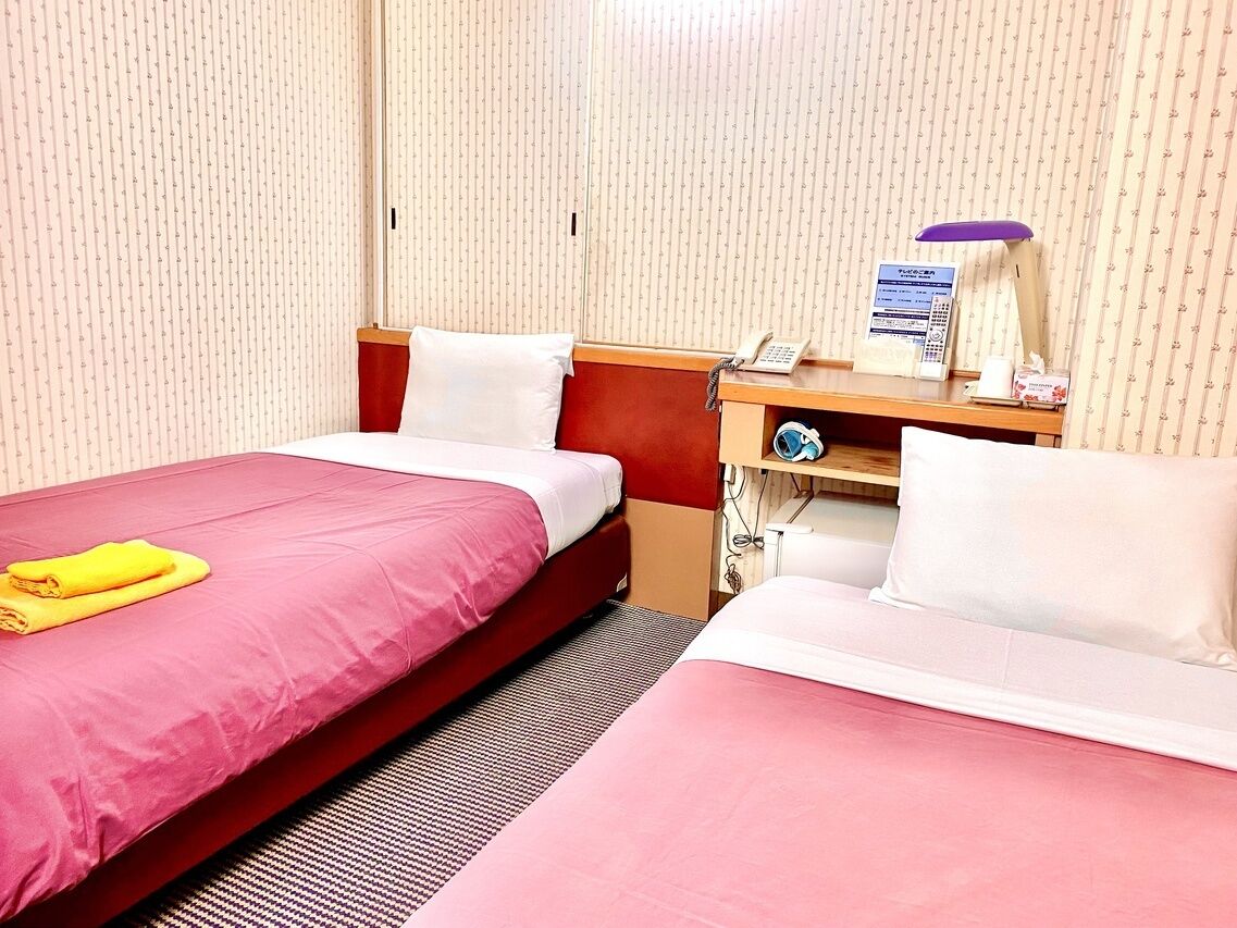 Habitación de hotel con dos camas, un escritorio con teléfono y un estante pequeño con artículos de tocador.