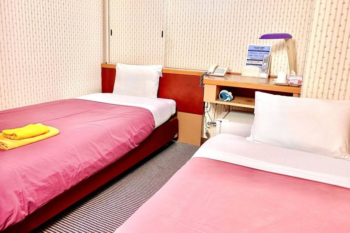 A hotel room with two beds, a desk with a telephone, and a small shelf with toiletries.