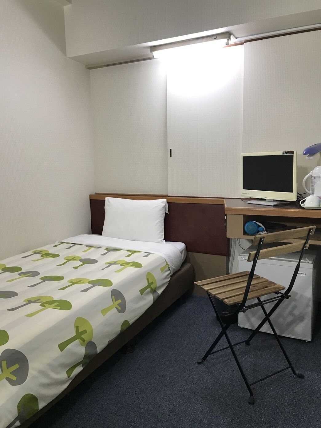 Una habitación de hotel con una cama, un escritorio con computadora, una silla y un refrigerador pequeño.